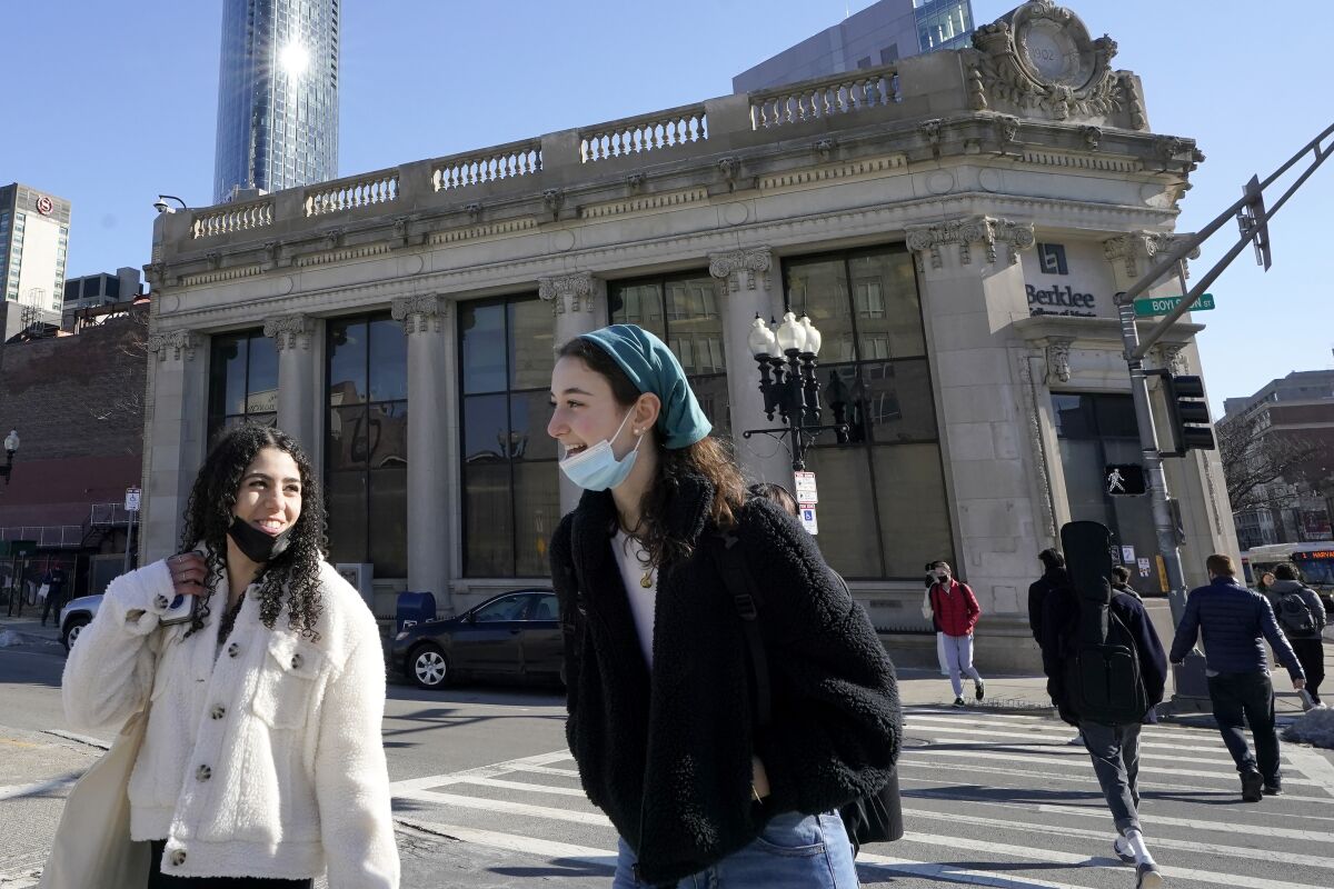 FILE - Passers-by wear masks under their chins as they chat with one another while crossing a street, in Boston, Wednesday, Feb. 9, 2022. Students and staff at public schools in Massachusetts will no longer be required to wear face coverings while indoors starting Feb. 28, state officials said Wednesday, Feb. 9, 2022. (AP Photo/Steven Senne, File)