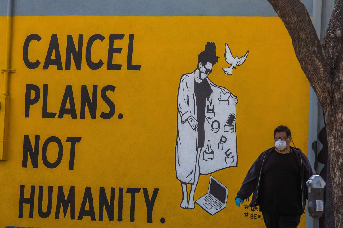 A man wearing gloves and a face mask walks by a mural in L.A. on Saturday.