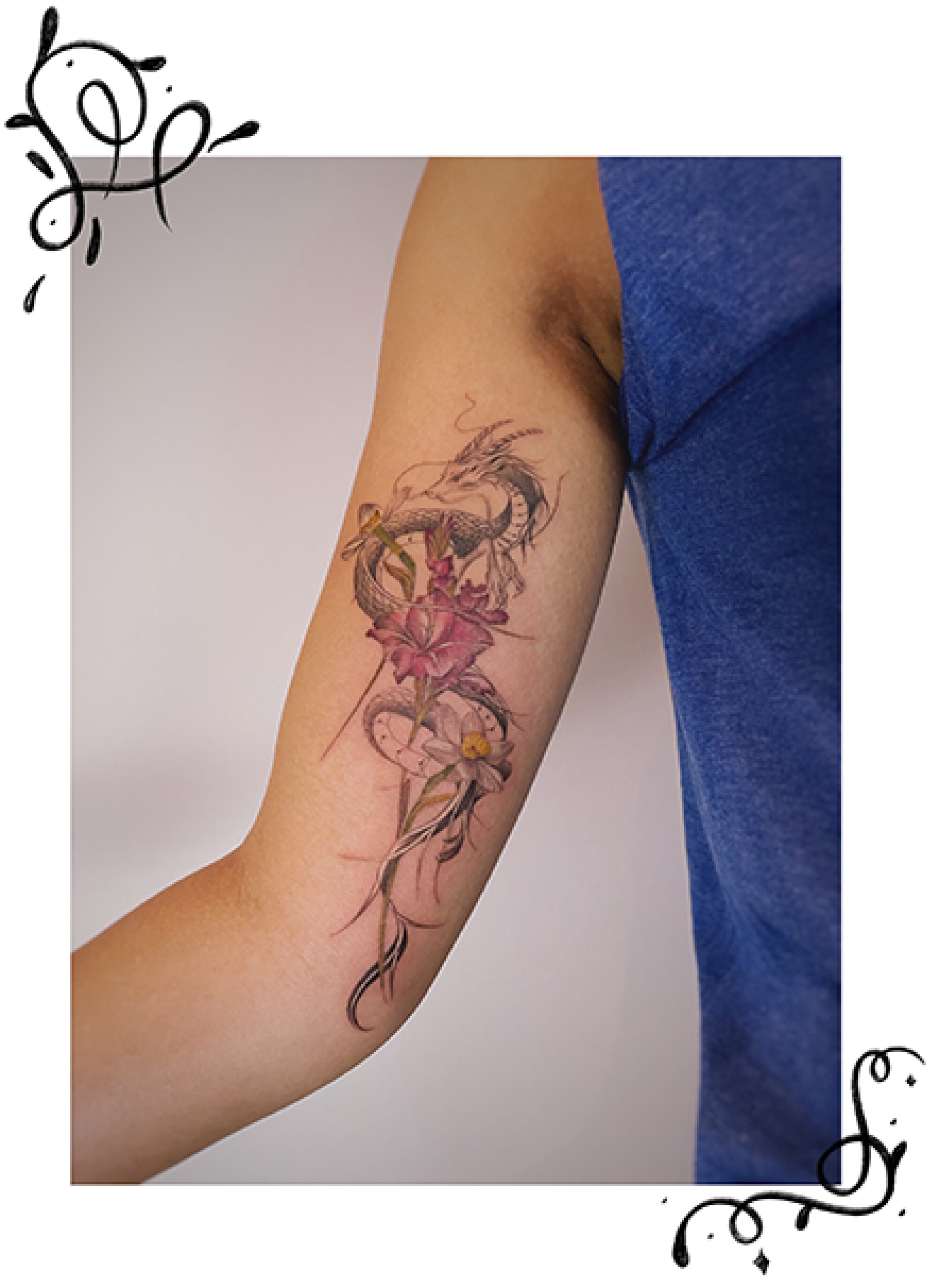 A tiny dragon flying with flowers tattoo on an arm.