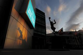 LOS ANGELES, CALIF. - APR. 10, 2020. The shadow of a statue of Magic Johnson, left, and a statue of Kareem Abdul Jabbar putting up a sky hook are frozen in time at Staples Center, where the lights are off and events have been suspended in the wake of the coronavirus pandemic. Wearing face cooverings now is mandatory in the city of L.A. as part of an ongoing effort to curb the spread of coronarivrus. (Luis Sinco/Los Angeles Times)