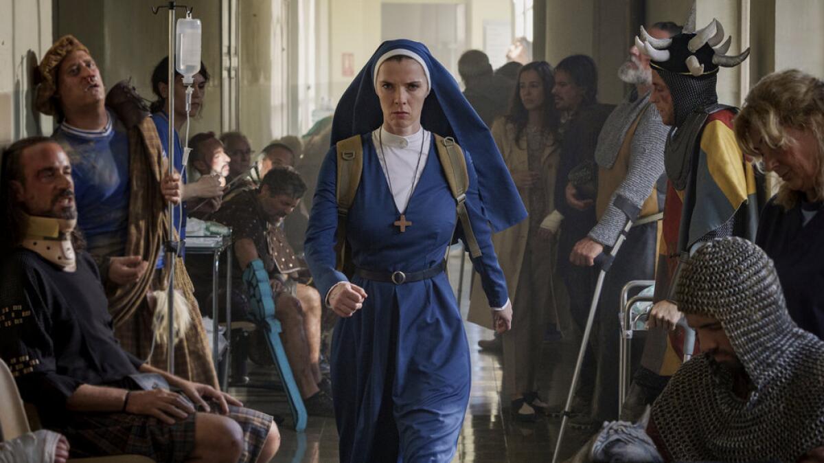 A nun in a blue habit walks through a hall lined with injured people in medieval dress.