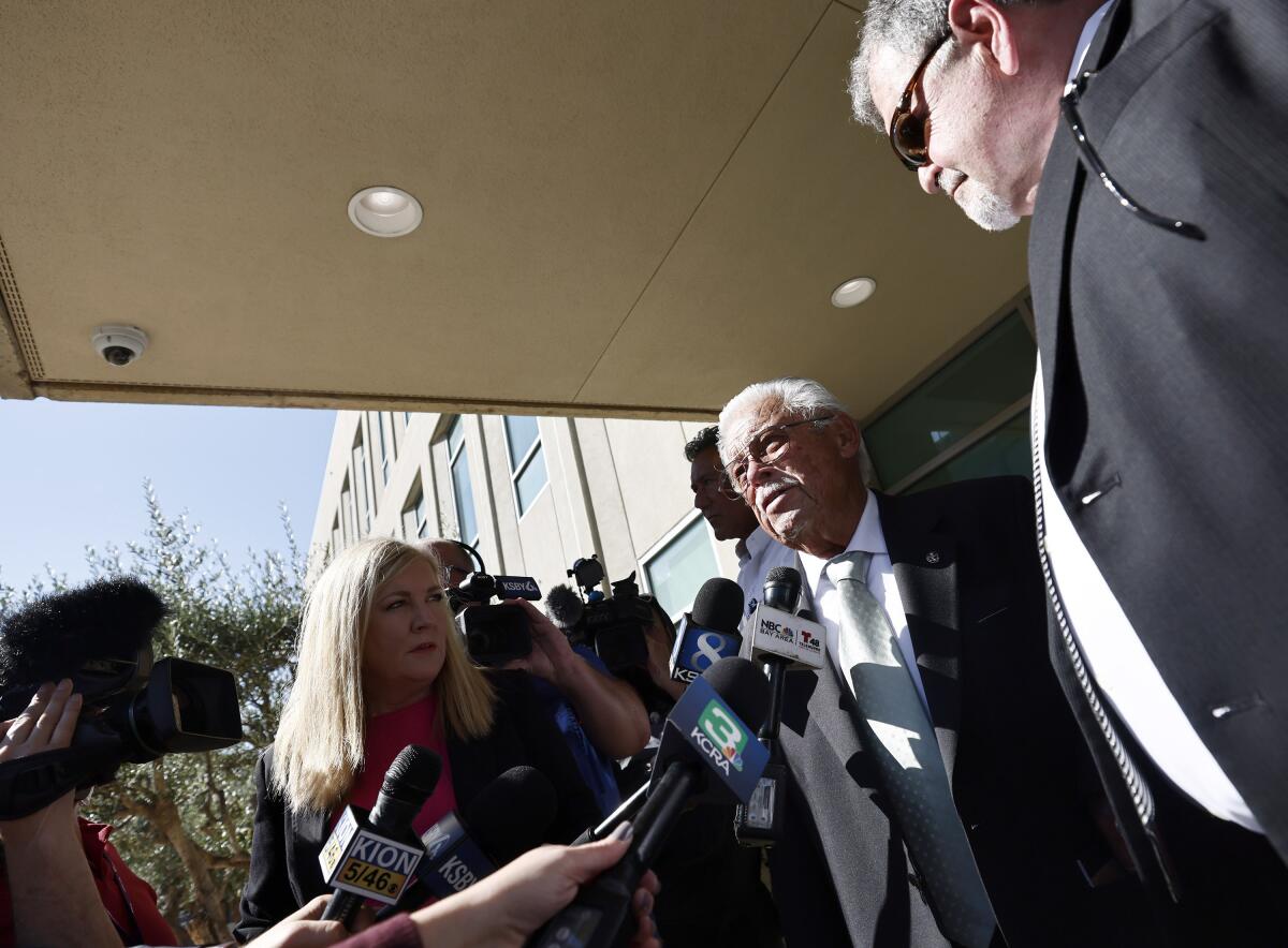 A man stands before a group of reporters holding microphones. 