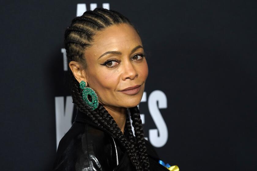 A woman with braided hair and large green earrings looks out of the corner of her eye