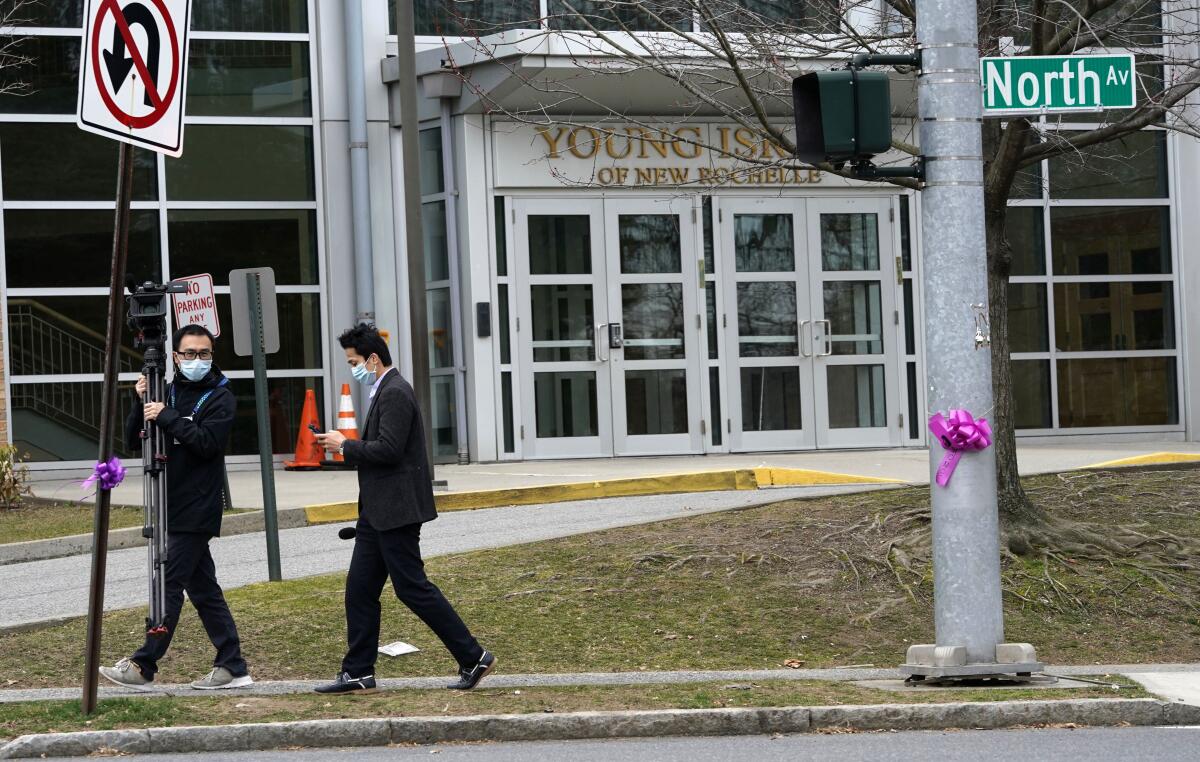 Media members wear masks as they film outside a synagogue in New Rochelle, N.Y., on Tuesday, where a one-mile containment zone will be set up with the hope of slowing down the coronavirus.