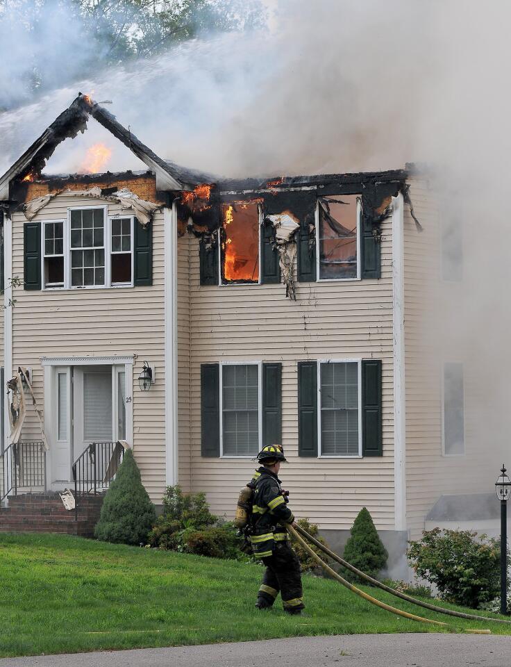 A firefighter moves a hose into position outside a house into which a small plane had crashed in Plainville, Mass., Sunday, June 28, 2015. Jim Peters of the Federal Aviation Administration says the Beechcraft plane crashed into the house at about 5:45 p.m. Sunday.