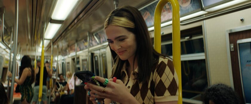 A woman in an argyle sweater looks at her phone while riding the subway