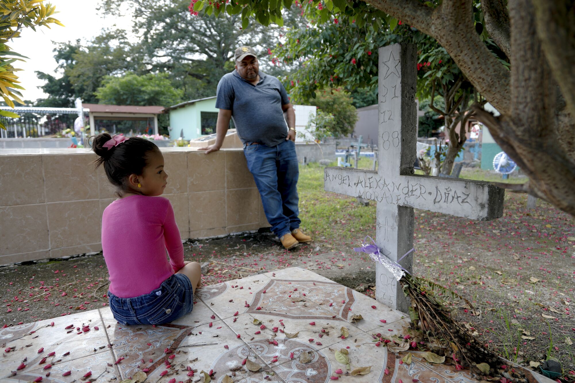 Angel Diaz's daughter Valery sits at his grave while her grandfather Alex Diaz Zavala stands nearby.