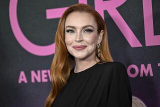 Lindsay Lohan wears a black dress as she smiles while posing for pictures at a red carpet event.