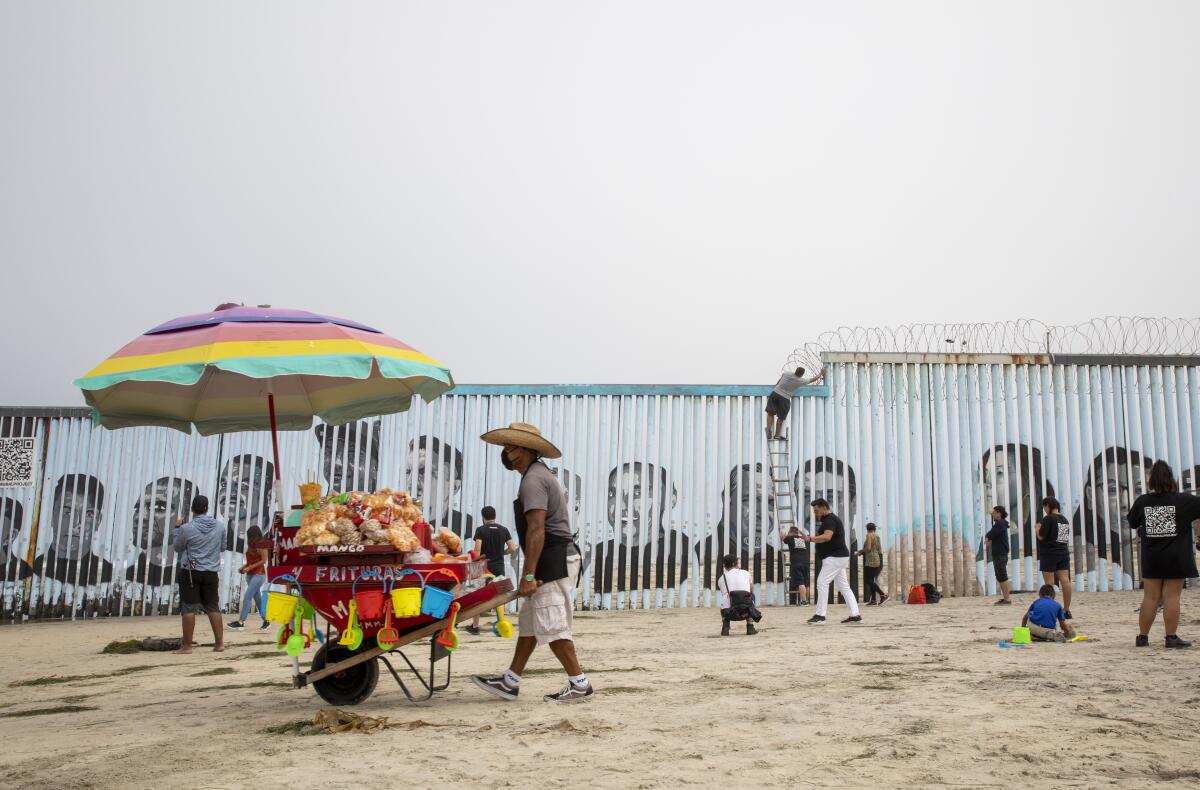 Un vendedor camina por la playa mientras se termina un nuevo mural fronterizo en Playas