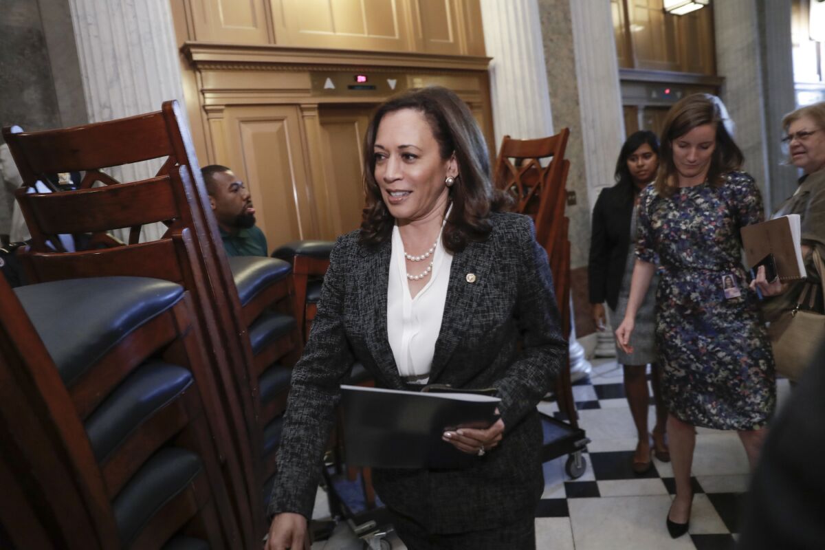 Sen. Kamala Harris, carrying a notebook, walks past stacked chairs.