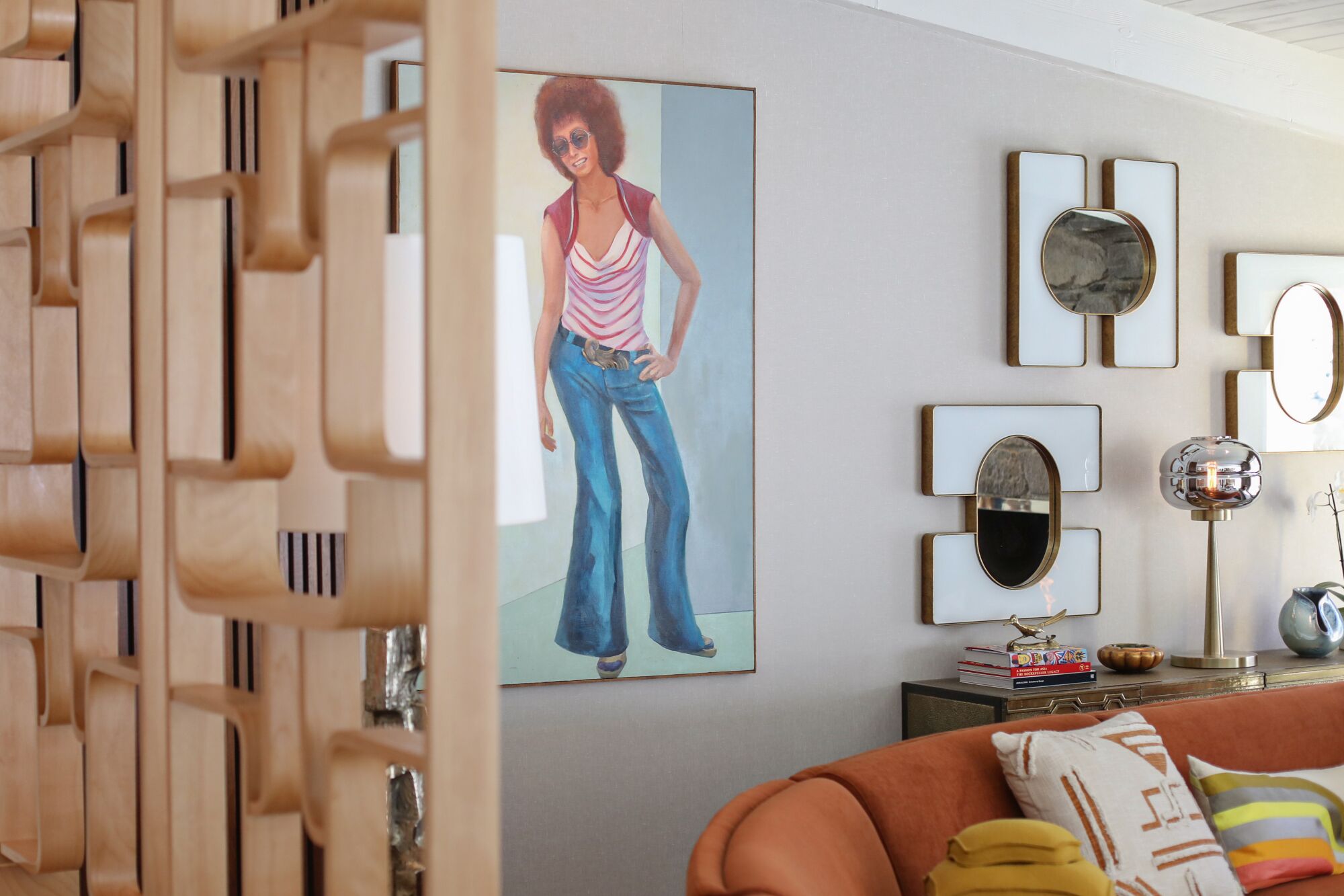 A painting of a woman on a wall, with a wooden room divider to the left and an orange couch to the right.