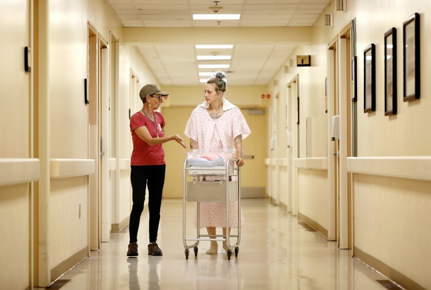 Two women walk in a hallway with a baby carrier