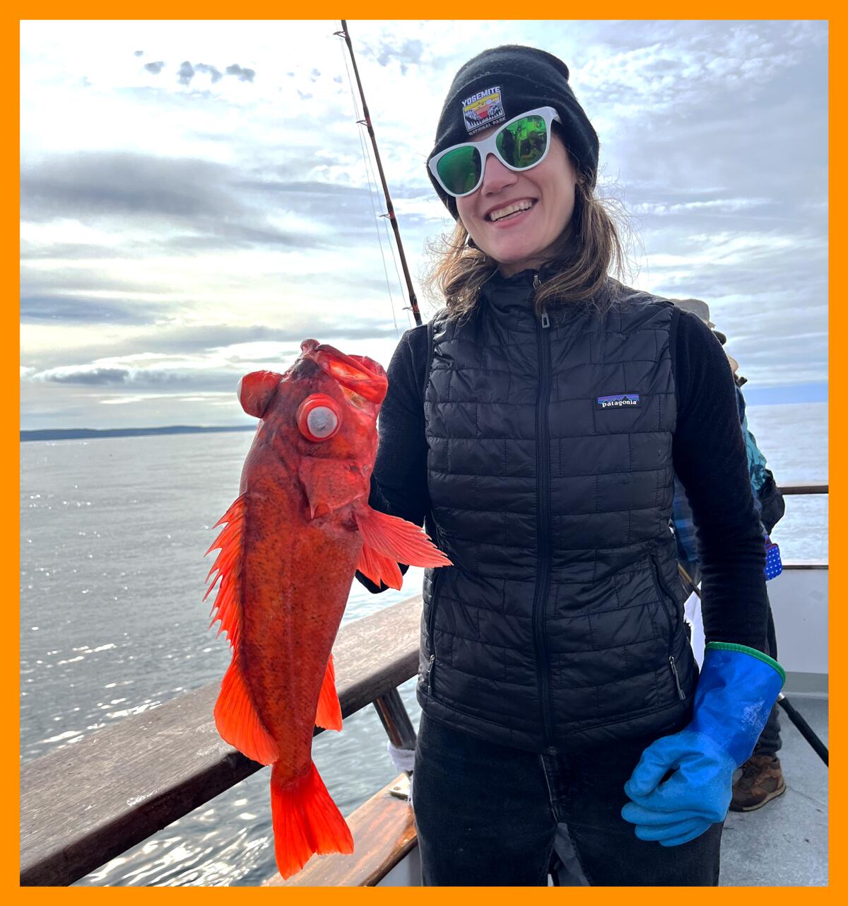 A woman wearing sunglasses holds a bright orange fish.