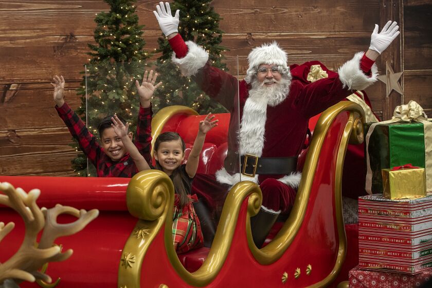 Los Angeles, CA -DECEMBER 11, 2020: Alexander Serrano, 10, left, and his sister Madison, 4, of West Covina, enjoy a photo opportunity with Santa Claus, safely separated from them by a piece of plexiglass, while aboard his sleigh at the Los Angeles Christmas Market on 3rd St. in Los Angeles. (Mel Melcon / Los Angeles Times)
