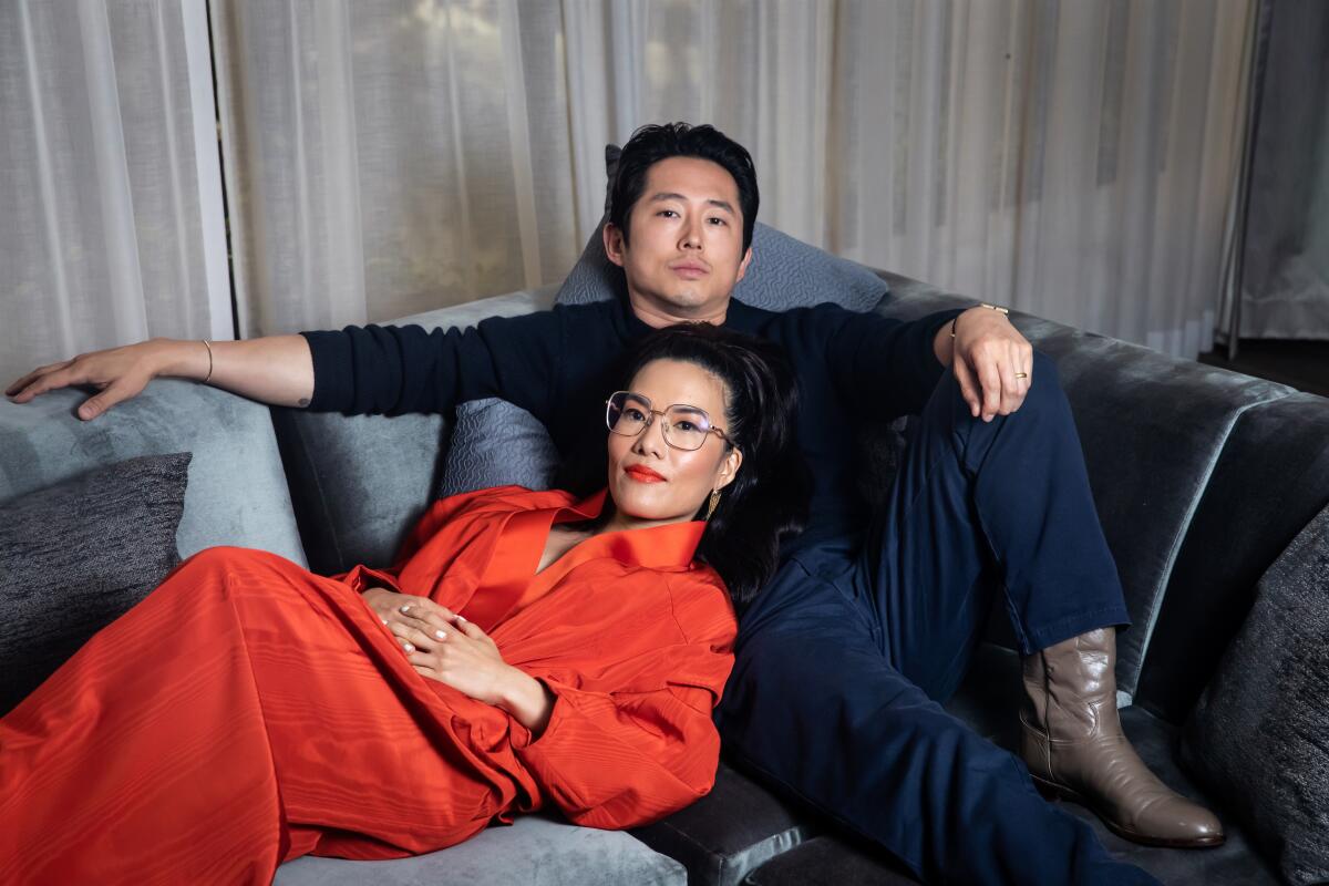 Ali Wong and Steven Yeun sit on a blue couch.