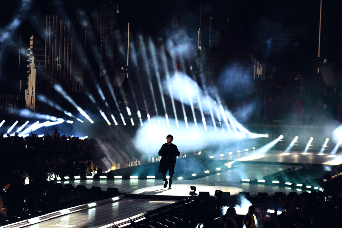 The silhouette of a singer appears on the Sofi Stadium stage with up-lights forming a dramatic backdrop.