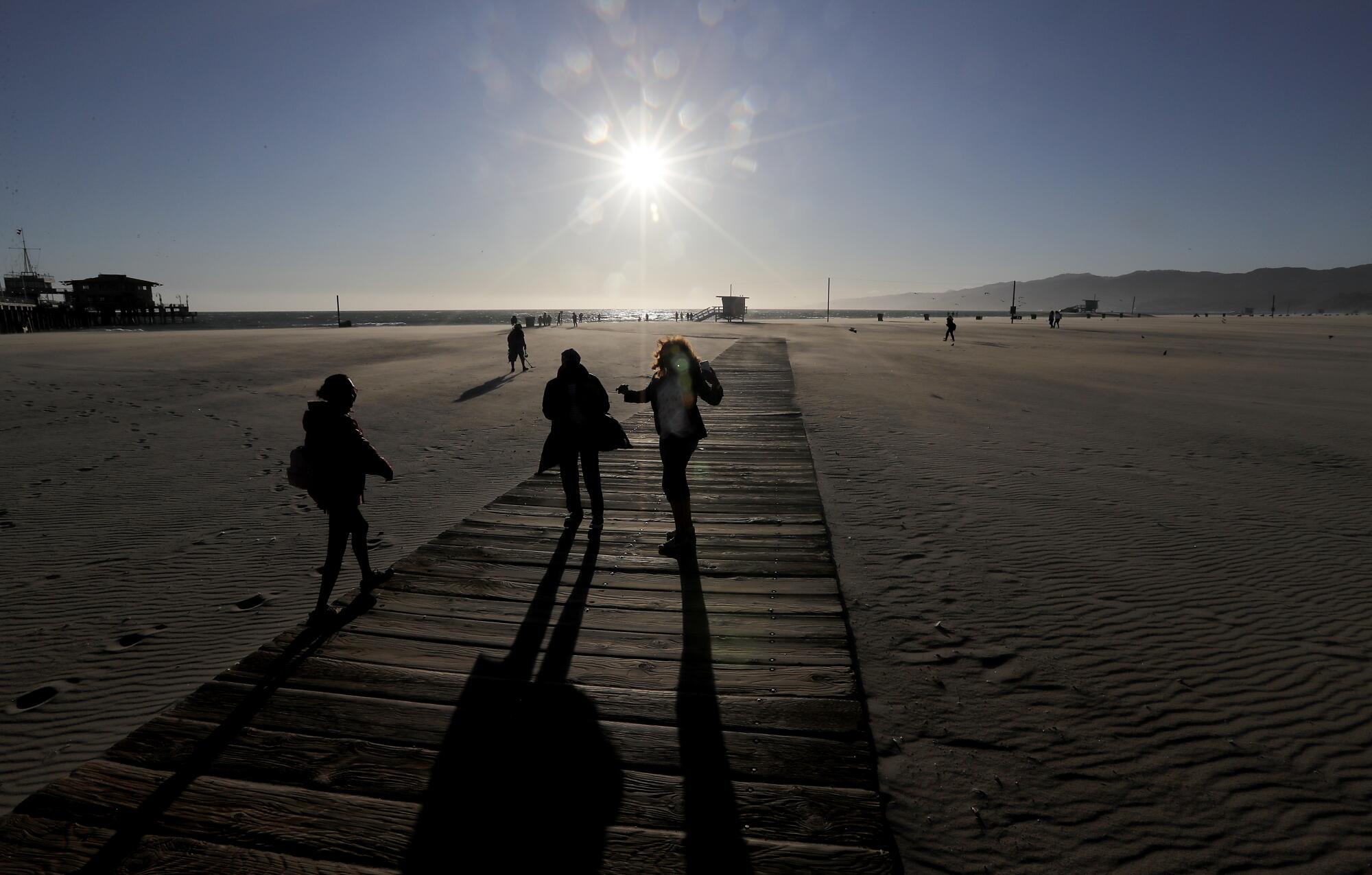 A handful of visitors walk on a largely deserted Santa Monica Beach.