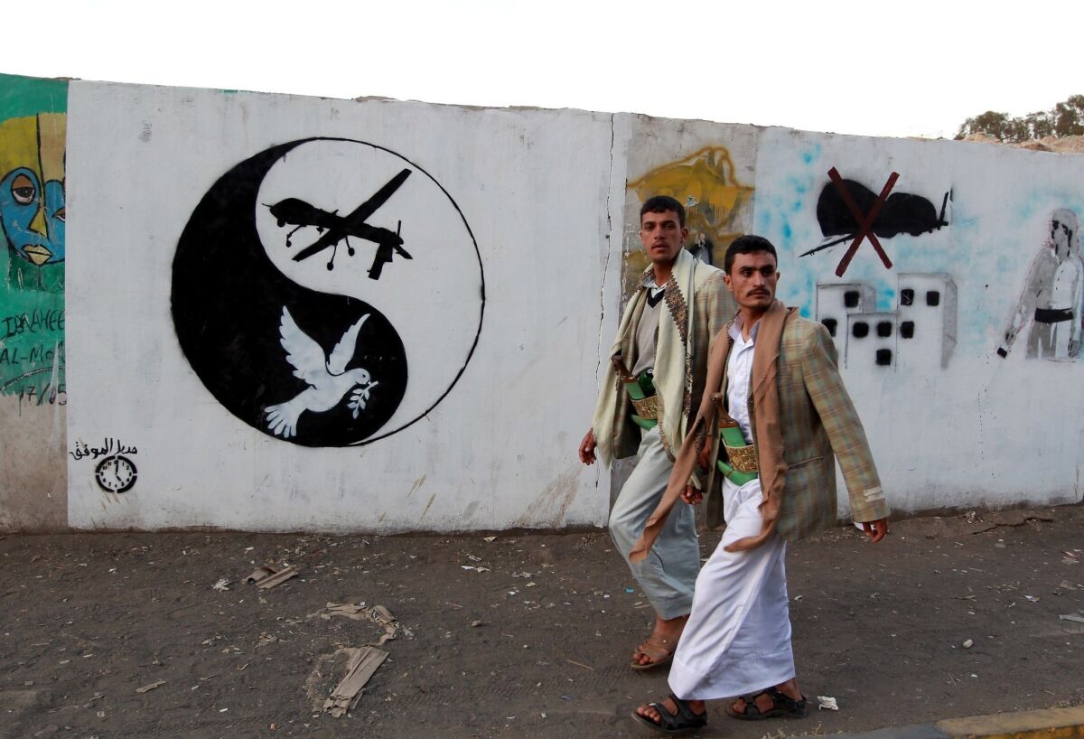 Yemeni men walk past a mural depicting a U.S. drone and a dove in a yin-yang symbol on Friday in the capital city of Sana.