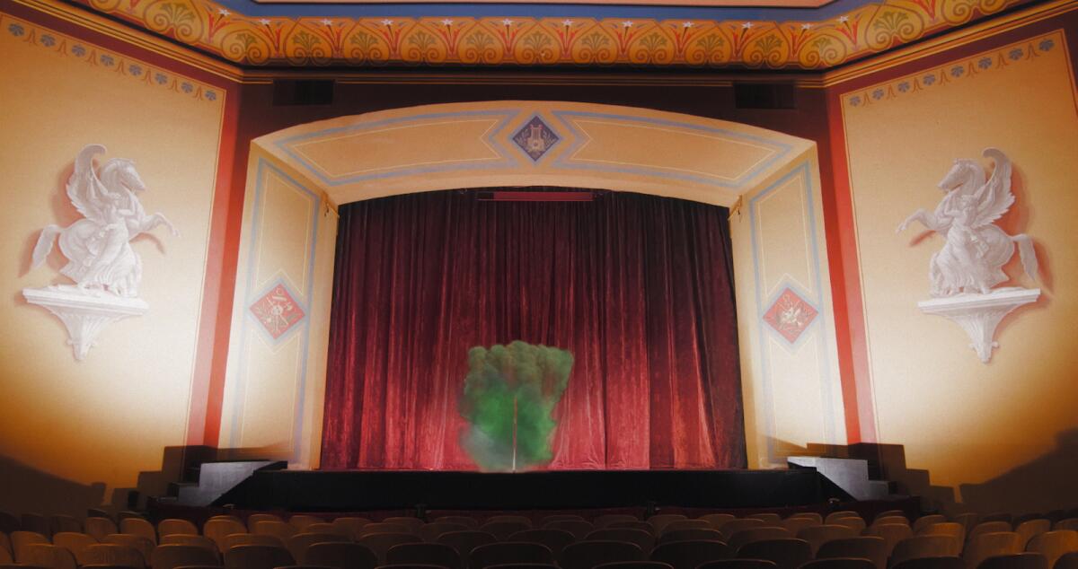 The interior of a theater, with red curtains in the framed proscenium opening