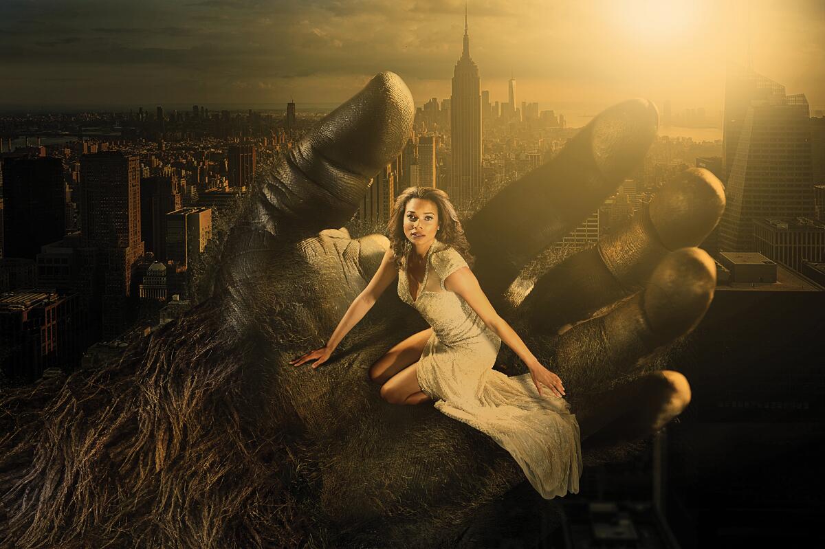 A woman sits in the palm of a giant ape hand, the Empire State Building in the background.