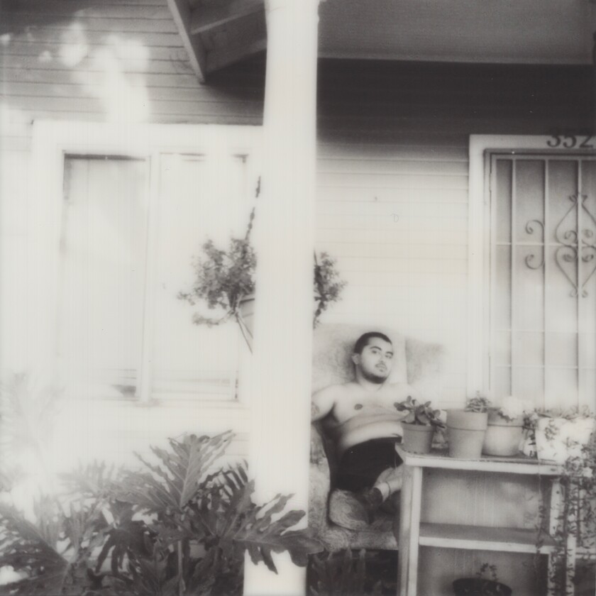 Xayn Nazerally sitting shirtless on their front porch surrounded by potted plants.