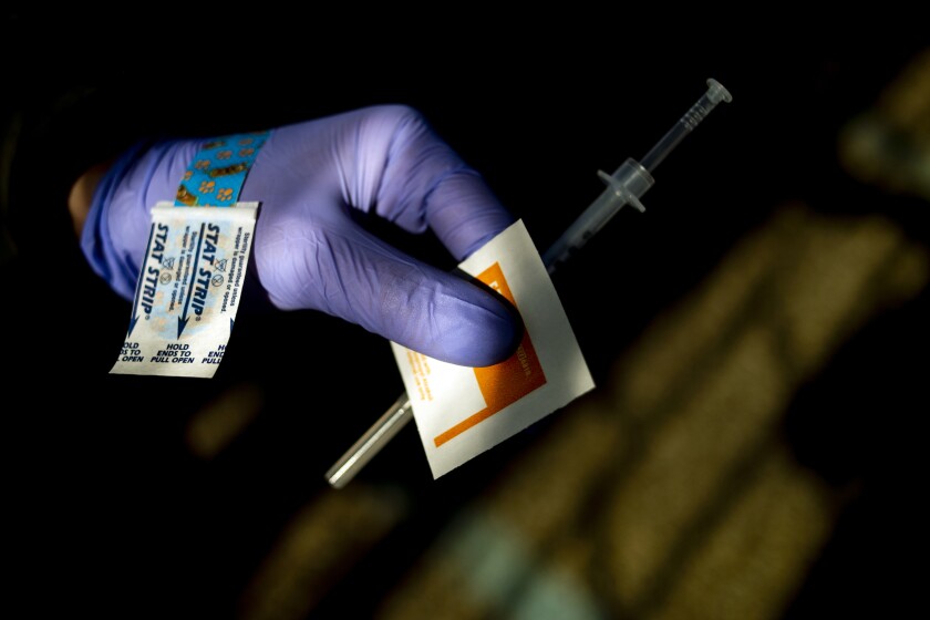 A gloved hand holds a needle and a disinfectant wipe