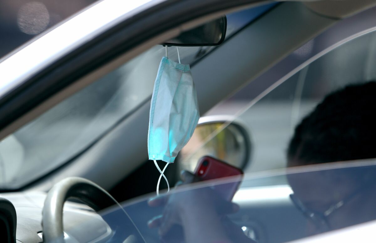 A mask hangs from a motorist's rearview mirror.