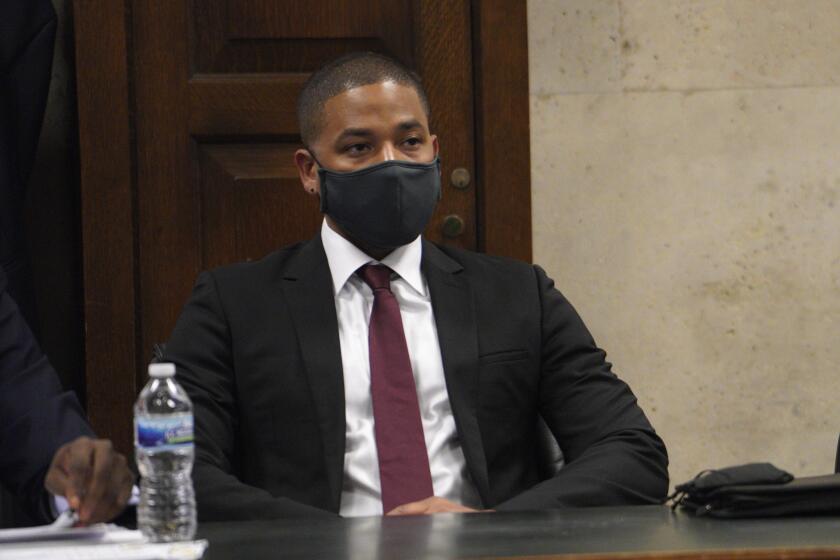 A man wearing a COVID-19 mask sits in a courtroom