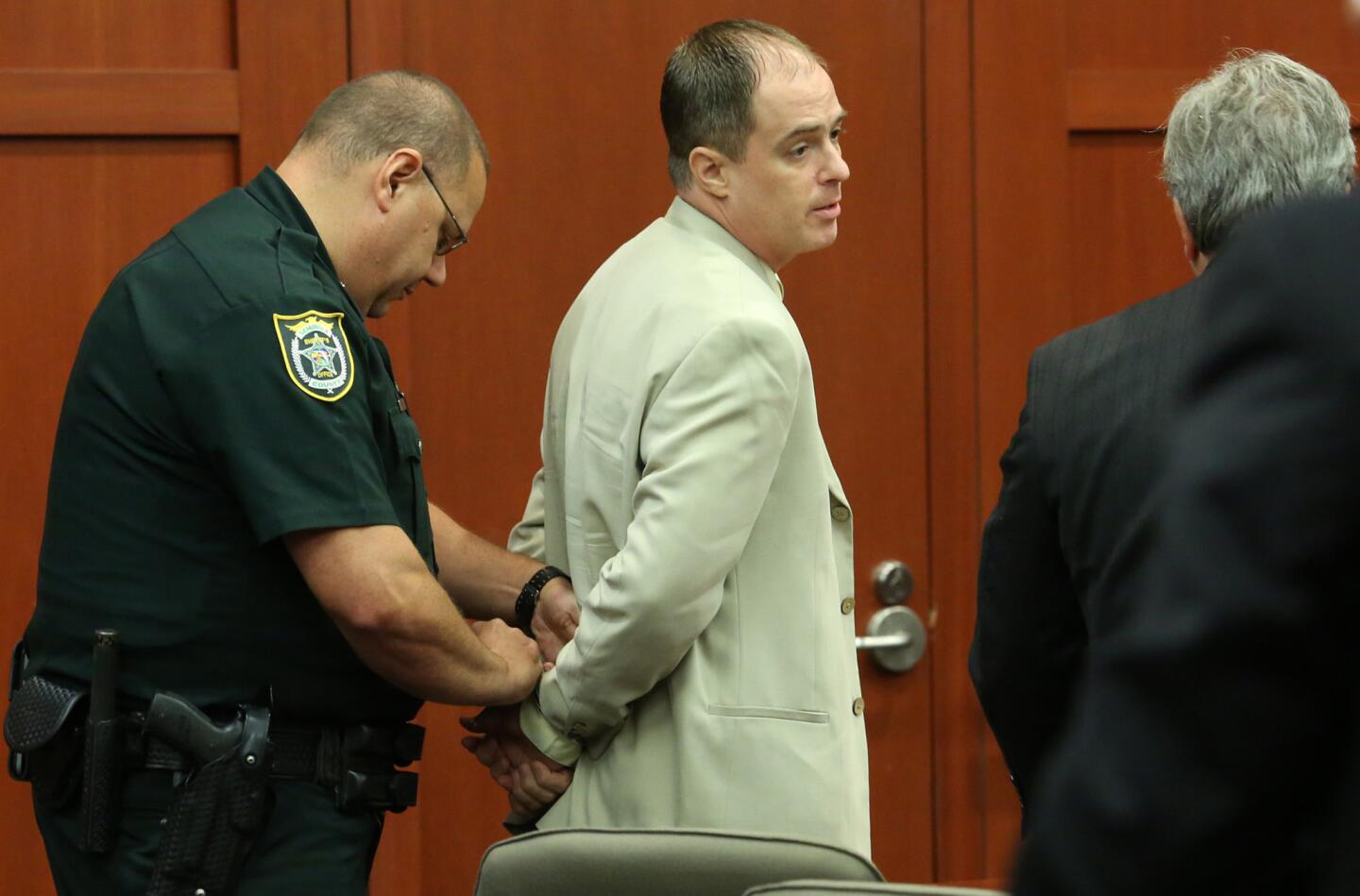 Matthew Apperson, center, confers with his attorney Michael LaFay,right, as he is handcuffed by a Seminole County Deputy Sheriff after Circuit Judge Debra S. Nelson ruled that because Apperson was charged with committing a new crime while free on bond Ð urinating on his neighbor's front door - he should be jailed. Apperson is the former mental patient who allegedly shot at Zimmerman in May in a road-rage incident at Lake Mary, Florida (Red Huber/Staff Photographer)