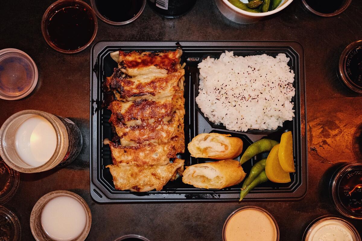 An overhead of a fried-gyoza bento box with rice, egg roll, and an array of sauces at Kaminari Gyoza Bar in Little Tokyo