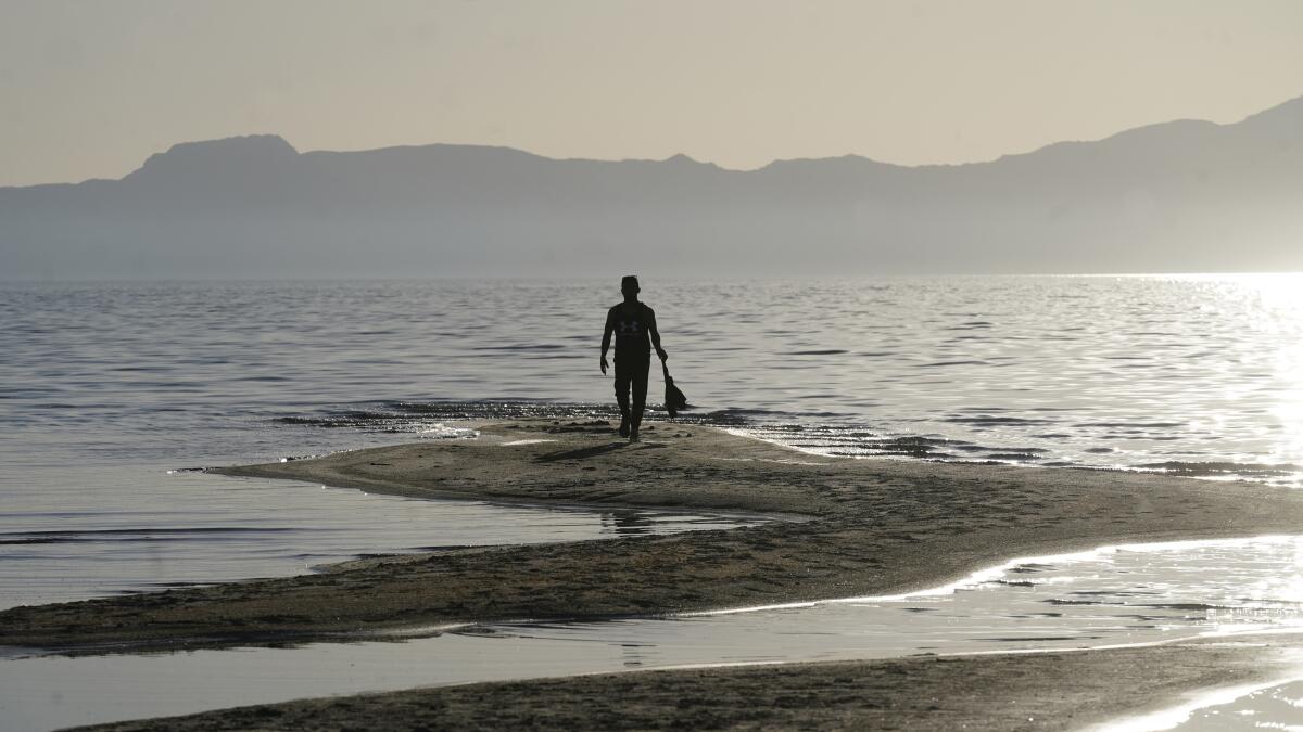 A man walks along a sand bar at the receding edge of the Great Salt Lake.