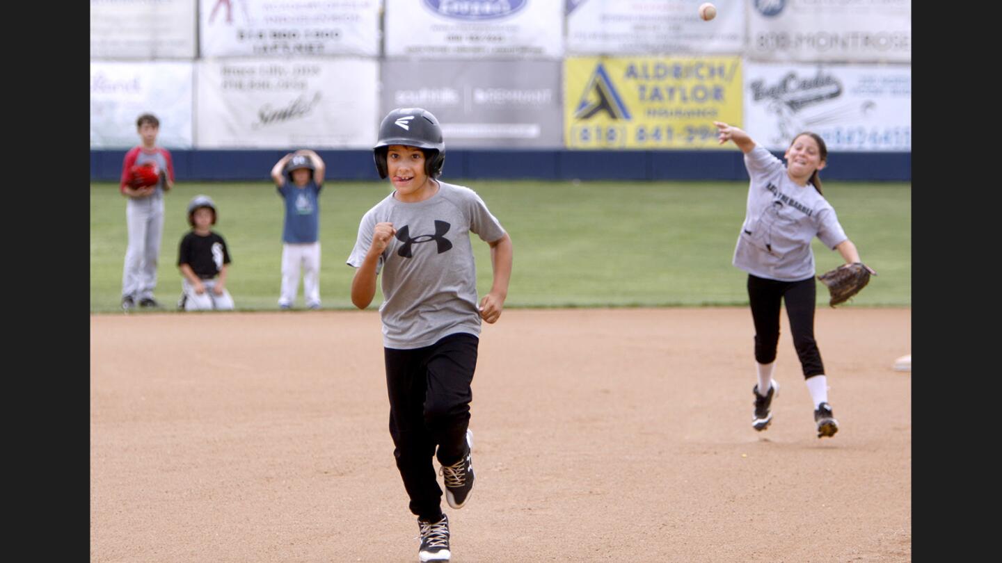 Preston Dumani, 9, tries to not get caught between second and third base as Bella Severo, 10, throws the ball, during the annual Bulldog Baseball Camp at Burbank High School, in Burbank on Wednesday, June 7, 2017.
