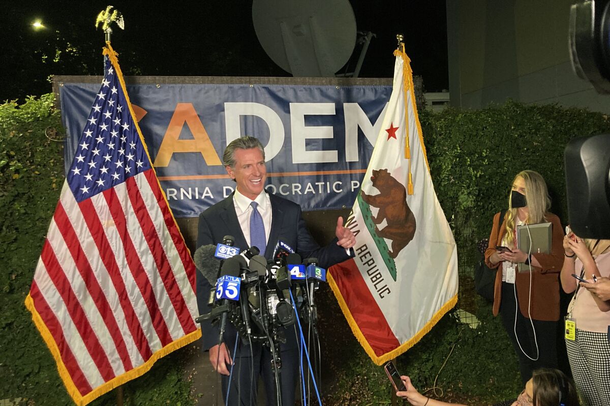 Gov. Gavin Newsom, flanked by flags, speaks into microphones