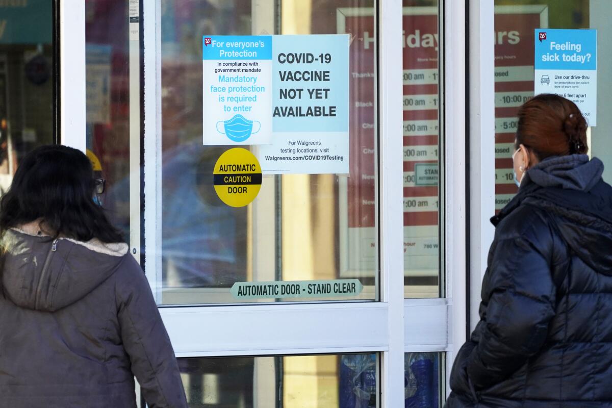 Customers in masks check out information signs that a COVID-19 vaccine is not yet available at Walgreens in Northbrook, Ill. 