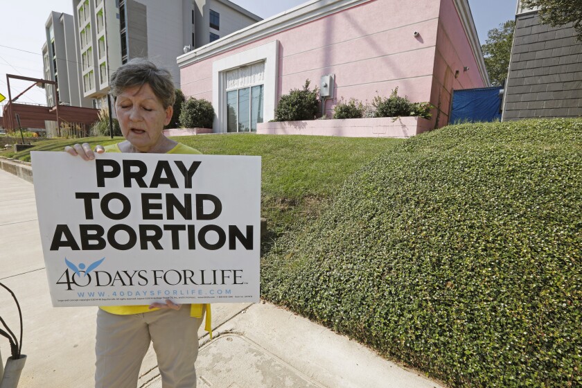 A woman holds a sign reading "Pray to end abortion" on a sidewalk outside a clinic 