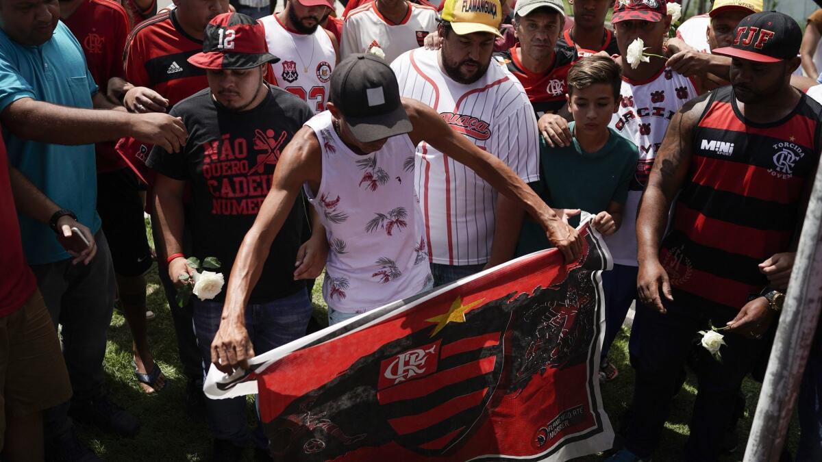 A fan holds a Flamengo flag during a vigil for the fire victims at the entrance of the soccer club's training complex in Rio de Janeiro.