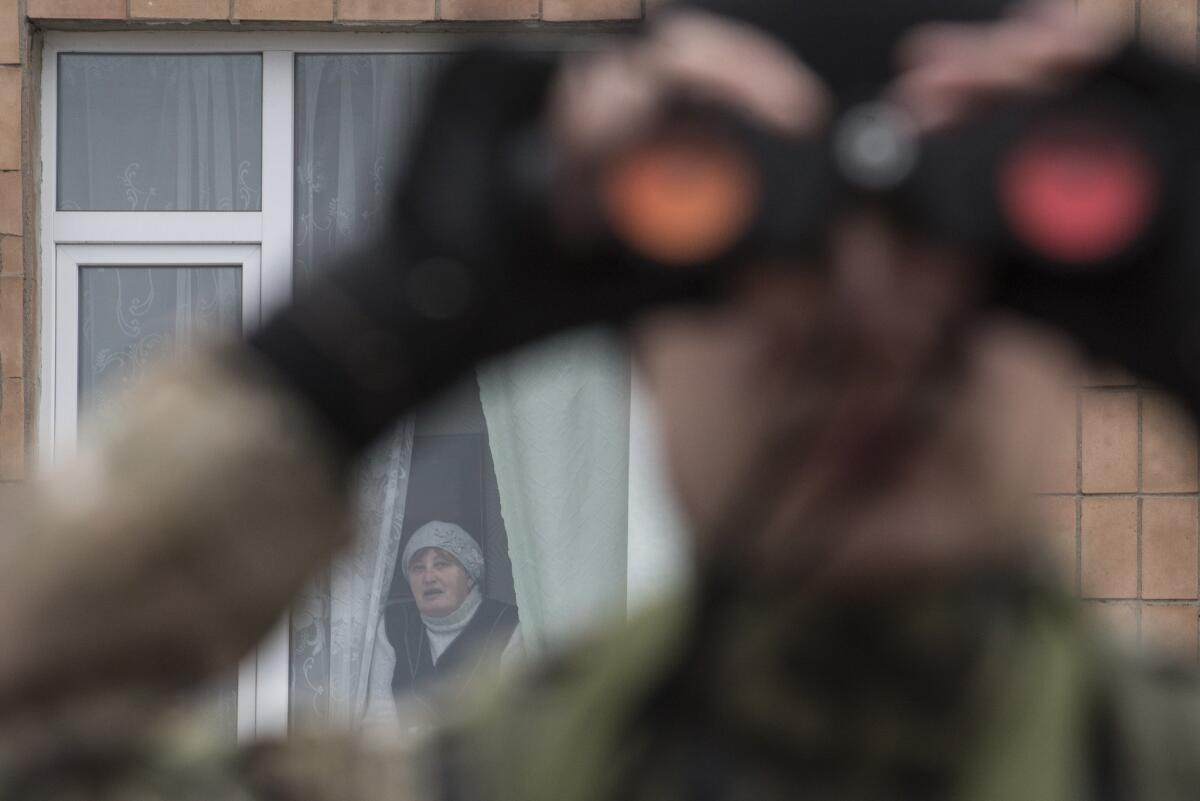 A Ukrainian soldier looks for evidence of a rebel pullback of heavy weapons in the village of Chermalyk in eastern Ukraine as a local woman watches from her apartment on Feb. 26.