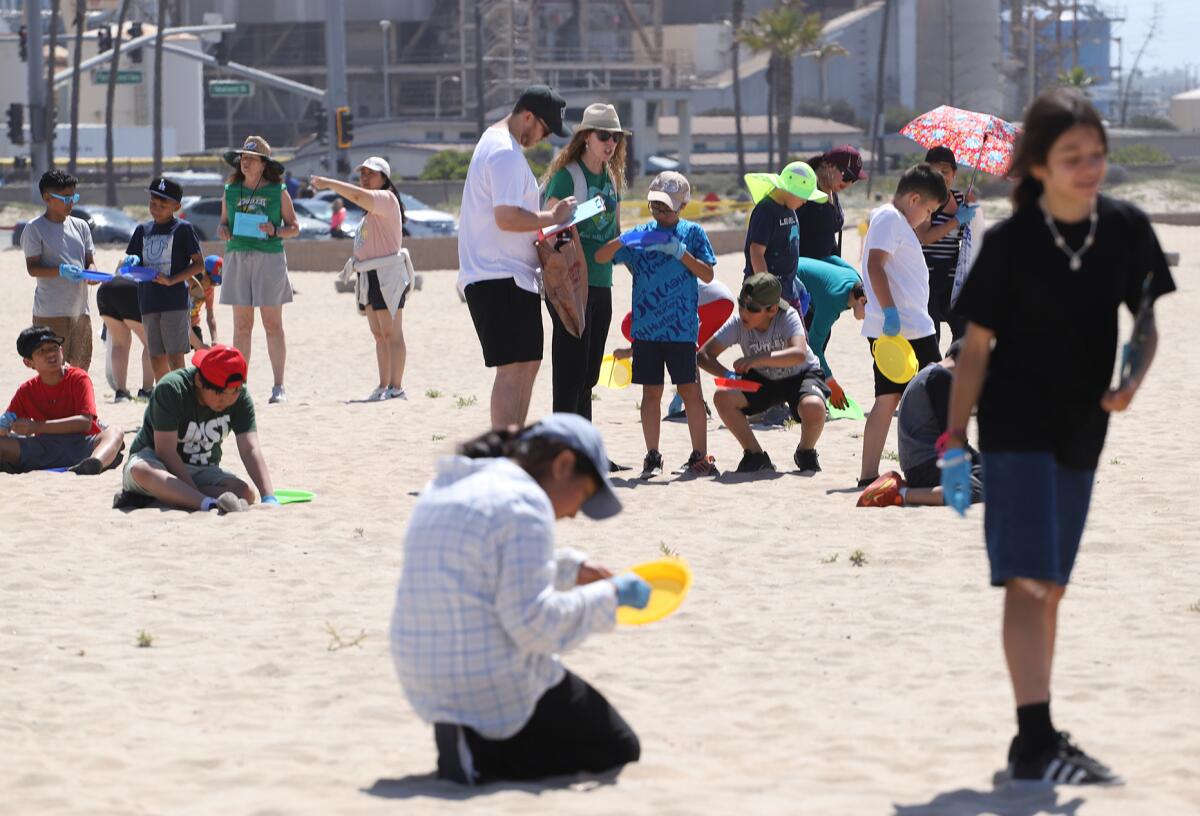 A group of Orange County elementary students sift through the sand to remove trash on Tuesday in Huntington Beach.