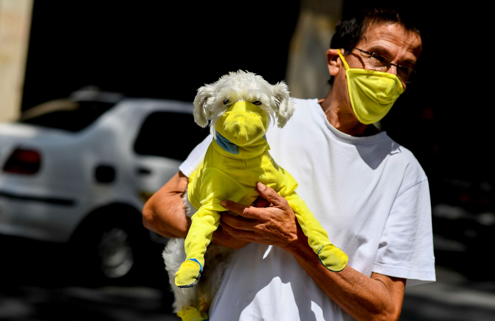 VENEZUELA: A man wears a face mask March 20 while he carries his dog with a protective suit as a preventive measure against the coronavirus spread in Caracas, Venezuela.