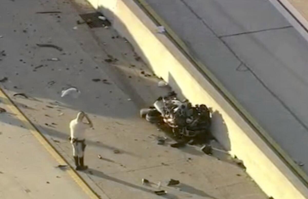 An investigator stands next to the mangled wreckage of a motorcycle lying against a freeway median.