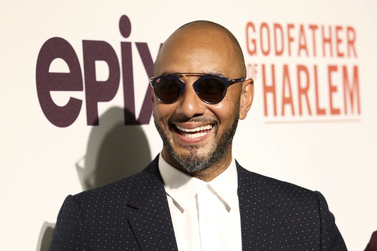 A man wearing sunglasses smiles in front of a banner.
