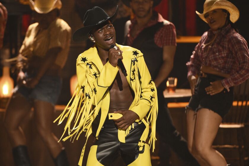 A man in a yellow fringe outfit and black cowboy hat singing into a microphone