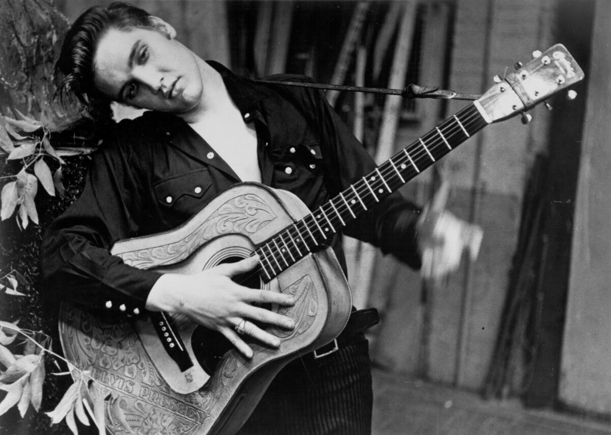 Elvis Presley poses for a portrait with a guitar in 1956.