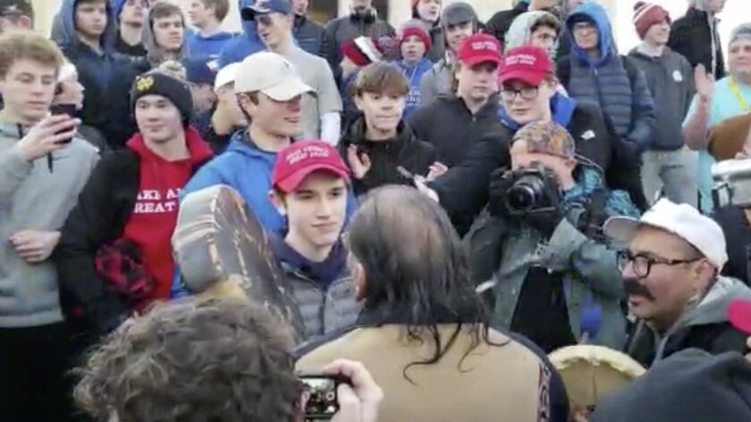 A teenager wearing a Make America Great Again hat, center left, stands in front of a Native American singing and playing a drum in Washington on Friday.