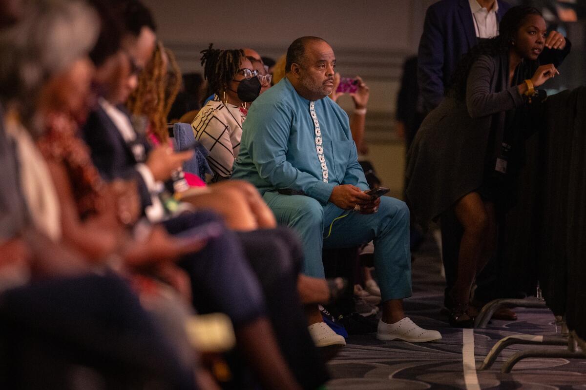 A man in a blue suit listens in the audience.