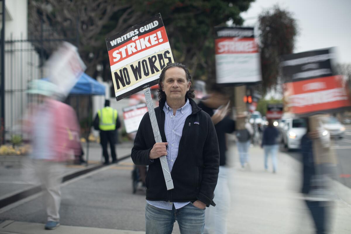 A man holds a picket sign as fellow picketers move behind him in blurred motion.