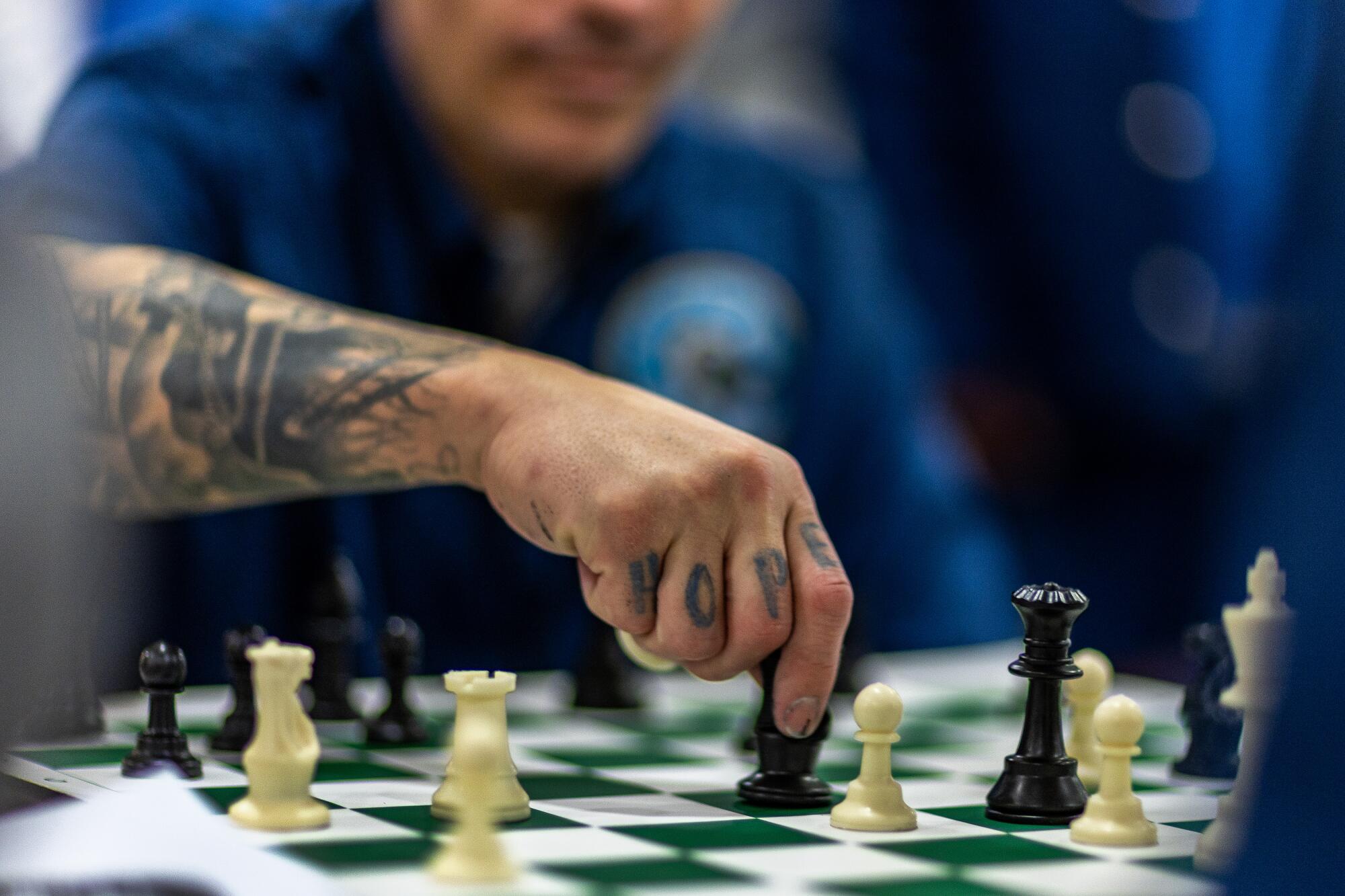 A tattooed man moves a chess piece.