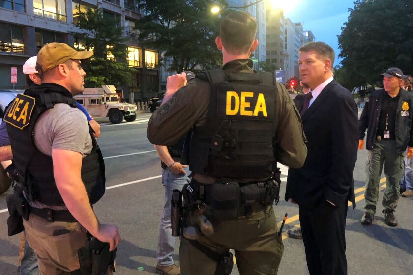 In this Wednesday, June 3, 2020, photo Acting Drug Enforcement Administrator Timothy Shea, right, visits with DEA agents at a checkpoint in Washington. More than 1,500 people have been arrested in the last three months as part of a Drug Enforcement Administration project focusing on violent crime. The initiative, nicknamed Project Safeguard, comes as President Donald Trump has touted similar operations as a much-needed answer to a spike in crime. It's also to showcase what he says is his law-and-order prowess, claiming he’s countering rising crime in cities run by Democrats. Acting DEA Administrator Tim Shea tells the AP that since the operation launched in August, 1,521 people have been arrested in both state and federal cases in cities across the U.S. and 2,135 firearms have been seized. (AP Photo/Mike Balsamo)