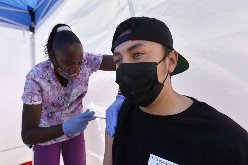 Los Angeles, California—May 12, 2021—At the East Los Angeles Civic Center, St. John’s Well Child & Family Center runs a vaccine clinic. Tanya Mitchell, a certified medical assistant, left, administers his a vaccinate to Richard Ayala, age 18, on California on May 12, 2021. (Carolyn Cole / Los Angeles Times)