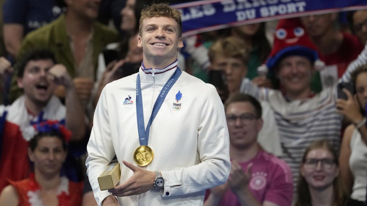 Leon Marchand of France grins as fans cheer after he received an Olympic gold medal.